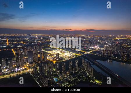 Aus der Vogelperspektive des Jiangxia District Wuhan China offenbart eine weitläufige Stadtlandschaft mit leuchtenden Lichtern, die Gebäude unter einem Dämmerungshimmel beleuchten. Stockfoto