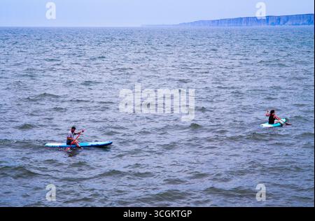 Ein paar Paddelboarder im abgehackten Wasser in Filey Bay Stockfoto
