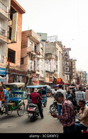 Rikscha-Fahrer, die durch eine belebte Straße in Paharganj, Delhi, Indien navigieren und Touristen vorbei an lebhaften Geschäften und Hotels unter einem hellen, Stockfoto