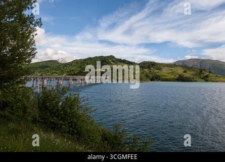 Eine Brücke über einen See mit Hügeln und einem schneebedeckten Berg in Italien Stockfoto