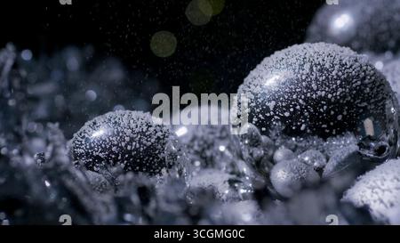 Blasen in verschiedenen Größen sind mit winzigen Tropfen bedeckt, während sie in einer schwach beleuchteten Umgebung glitzern. Stockfoto