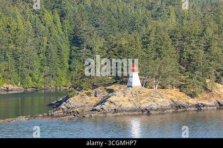 Ein kleiner weißer Leuchtturm mit rotem Dach auf der felsigen Insel nahe Vancouver Island Kanada, umgeben von Kiefernwäldern. Reisefoto, niemand Stockfoto