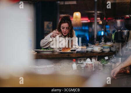 Frau genießt eine Mahlzeit an einem gemütlichen Restauranttheke mit lebhaftem Ambiente Stockfoto