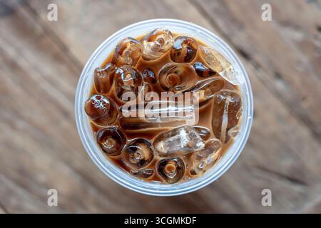 Blick auf Eiskaffee oder Latte von oben auf hölzernem Hintergrund. Schwarzer Kaffee mit Eis in Plastikglas, Nahaufnahme Stockfoto