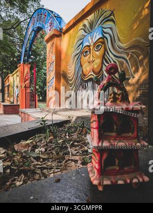 April 29th2025 Dehradun Uttarakhand Indien. Farbenfrohes Wandbild von Hanuman an einer Tempelwand mit einem kleinen Schrein im Vordergrund. Stockfoto