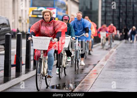 Menschen schützen sich vor Regen in wasserdichten Mänteln, während sie während eines Regenschusses durch Westminster im Zentrum Londons fahren. Bilddatum: Freitag, 29. August 2025. Stockfoto