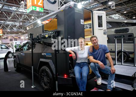 Düsseldorf, Deutschland. August 2025. Fotomodelle sitzen auf dem abnehmbaren Wohnmobil „Cyberjoy“ für den Tesla Cybertruck, der auf der „Caravan Salon – Fachmesse für Caravaning, Camping und Outdoor-Tourismus“ auf dem Stand der Firma „Hotomobil“ zu sehen ist. Bis zum 7. September werden mehr als 810 Aussteller das Branchenangebot in 15 Messehallen und auf dem Freigelände präsentieren. Quelle: Henning Kaiser/dpa/Alamy Live News Stockfoto