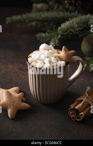 Weihnachtskaffee mit Marshmallow und Keksen als Schneemann in brauner Tasse auf dunklem Hintergrund. Weihnachten gemütlicher Urlaub. Vertikales Format. Stockfoto