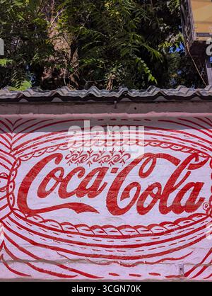 März 29.2025 Dehradun Uttarakhand Indien. Rot-weißes Coca-Cola-Wandgemälde auf einer Ziegelwand mit dekorativen Mustern. Stockfoto