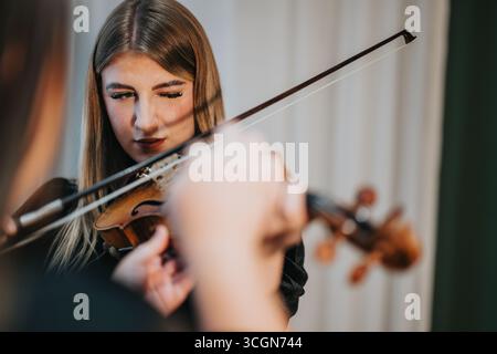 Junge Frau, die sich konzentriert, während sie in Nahaufnahme aufmerksam Geige spielt Stockfoto