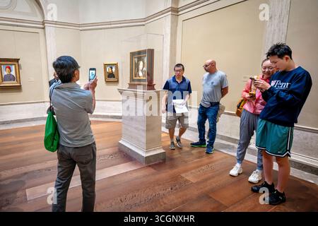 Leonardo da Vincis Ginevra de Benci in der National Gallery of Art in Washington DC // WASHINGTON DC – Besucher sehen und fotografieren Leonardo da Vincis Ginevra de Benci in der National Gallery of Art Das Gemälde mit Öl auf Holztafeln, das um 1474–1478 entstand, zeigt Ginivra de' Benci, eine junge florentinische Frau aus einer prominenten Bankenfamilie, und ist das einzige Gemälde von Leonardo da Vinci, das in Amerika öffentlich ausgestellt wird. Das Porträt zeigt Leonardos innovative Techniken, einschließlich der Verwendung von Sfumato und der detaillierten Darstellung der Haare des Motivs und des wacholderstrauchs hinter ihr, der weiterspielt Stockfoto