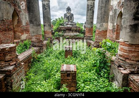 Yadana Hsemee Pagode Komplex Buddha Statue Ruinen Apyin Sanyar Dorf Myanmar // MANDALAY REGION, Myanmar - Eine ruinierte Buddha Statue ist inmitten der Ziegelsteinmauern und bewachsenen Vegetation des Yadana Hsemee Pagode Komplexes (ရတနာဆီမီးဘုရားစု) im Dorf Apyin Sanyar zu sehen. Diese bedeutende historische und religiöse Stätte in Inwa (auch bekannt als Ava) zeigt frühe Ziegelarbeiten im Konbaung-Stil und Buddha-Bilder. Der antike Komplex umfasst sechs Stupas, ein Backsteinkloster und drei Gandhakuti-Hallen, die aus zehn architektonisch wichtigen Bauten bestehen (nummeriert von 372 bis 381). Westlich des alten Ava-Palastes gelegen Stockfoto
