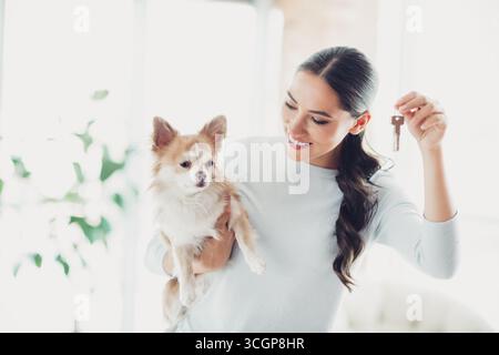 Lächelnde Frau mit Schlüsseln und bezaubernder Chihuahua Hund in einem hellen, modernen Innenraum Stockfoto