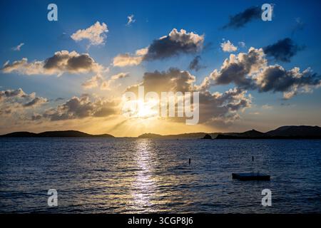 Sonnenuntergang über St. Thomas vom Gallows Point Cruz Bay St. John USVI // St. JOHN, USVI — Ein Sonnenuntergang wirft goldene Strahlen durch Wolken über der Insel St. Thomas in der Ferne, vom Gallows Point in Cruz Bay aus gesehen. Die Szene fängt die ruhigen Gewässer der amerikanischen Jungferninseln in der Abenddämmerung ein. St. John ist eine der Hauptinseln im US-Virgin Islands-Archipel. Stockfoto