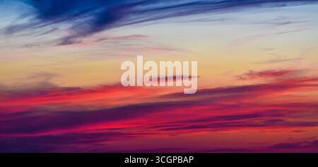 Traumhafte Wolken, die von verborgenem Sonnenuntergangslicht beleuchtet werden und den Himmel mit lebhaften Farben und friedlicher Magie der Dämmerung bemalen. Stockfoto