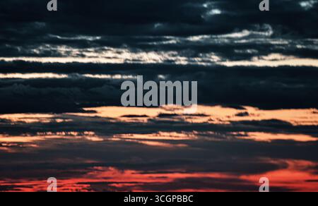 Ruhiger Sonnenuntergang mit leuchtenden Himmelsfarben und schwebenden Wolken, die eine bezaubernde, magische Abendlandschaft schaffen. Stockfoto