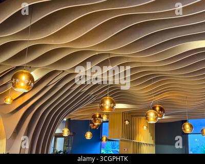 Dekorative Decke mit goldenen Lampen und welliger Holzstruktur im modernen Restaurant. Atmosphäre, Architektur, Gastfreundschaft und zeitgenössisch Stockfoto