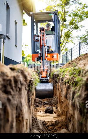 Minibagger, der einen Graben neben einem Haus aushebt Stockfoto