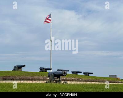 Eine Reihe historischer Küstenverteidigungskanonen säumt die grasbewachsenen Stadtmauern von Fort Macon in North Carolina mit amerikanischer Flagge Stockfoto
