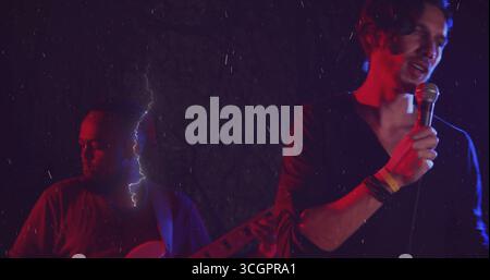 Singender Sänger, der Armbänder trägt und ein Mikrofon auf der Bühne hält, während der Gitarrist E-Gitarre spielt Stockfoto