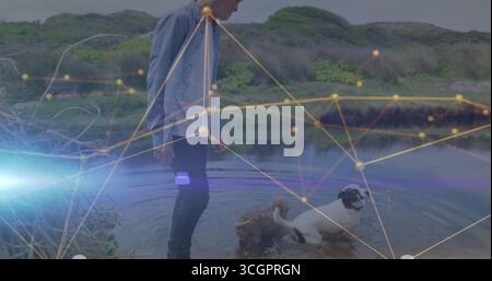 Stehender Mann mit blauem Hemd, dunkler Jeans im Bach, mit zwei Hunden im Wasser, Netzwerküberzug Stockfoto