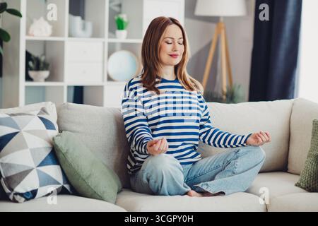 Junge Frau übt Entspannungstechniken auf einer gemütlichen Couch zu Hause in einem wunderschön eingerichteten Wohnzimmer Stockfoto