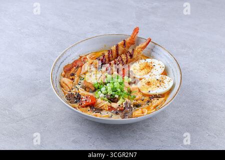 Nahaufnahme authentischer japanischer Ramen mit knusprigen gebratenen Garnelentempura, gekochtem Ei, Zwiebeln, Pilzen, Tomaten, und Nudeln in reichhaltiger Brühe, serviert mir Stockfoto