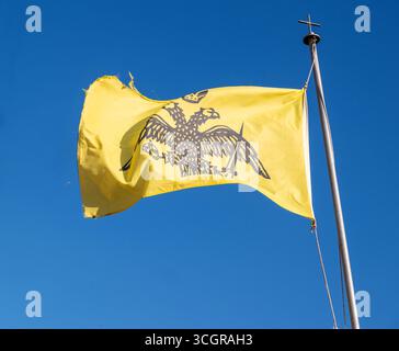 Das byzantinische Reich und die griechisch-orthodoxe Kirchenflagge winken auf blauem Himmel. Doppelköpfiger Adler auf gelb Stockfoto
