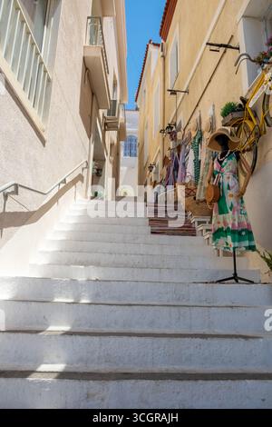 Pfeiltreppe in Poros Inselstadt, Griechenland. Kleiderständer, Kleider und Accessoires für Damen, Blick aus flachem Winkel, blauer Himmel Stockfoto