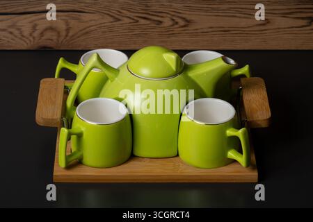 Ein grünes Teekannen-Set aus Keramik mit einem einzigartigen Design und vier passenden Bechern, die die skulpturalen Überstände des Topfes spiegeln, die auf einem Tisch angeordnet sind. Stockfoto