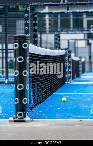 Paddle-Tennisball, der auf der blauen Kunstrasenoberfläche eines Paddle-Tennisplatzes liegt, in der Nähe des Netzes Stockfoto
