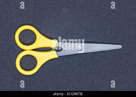 Leichte Schere mit gelbem Griff für Handwerk und Büro auf dunklem Hintergrund Stockfoto
