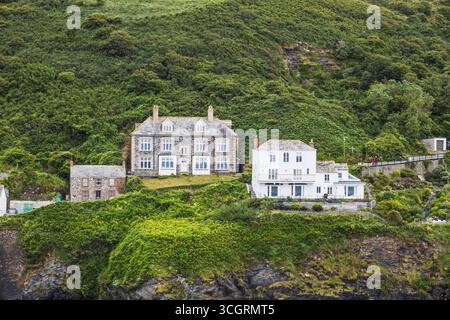 Küstenhäuser auf Klippen auf üppig grünen Hügeln, zerklüftetes Küstendorf, malerische Küste Großbritanniens Stockfoto