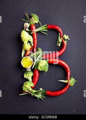 Kreativer Buchstabe B aus Chilischoten, Brokkoli, Rosmarin, Tomaten und Olivenöl auf dunklem Hintergrund. Einzigartige Essenstypografie für kulinarisches Design Stockfoto