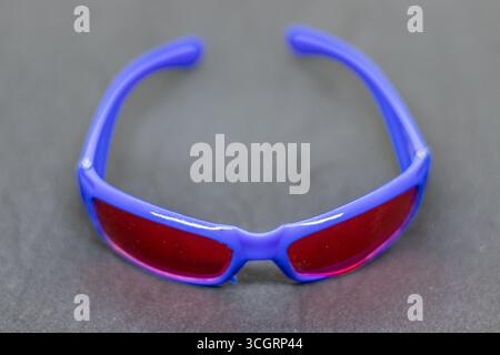 Stilvolle Sonnenbrille mit blauem Rahmen und rot getönten Gläsern auf dunklem Hintergrund Stockfoto