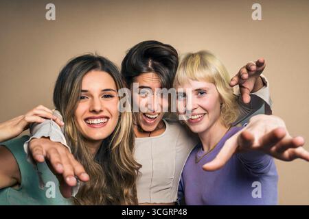 Verspieltes Studio-Porträt von drei verschiedenen und glücklichen jungen Frauen, die ihre Hände in einer lustigen und einladenden Geste zur Kamera strecken, als wollten sie "gut" sagen Stockfoto