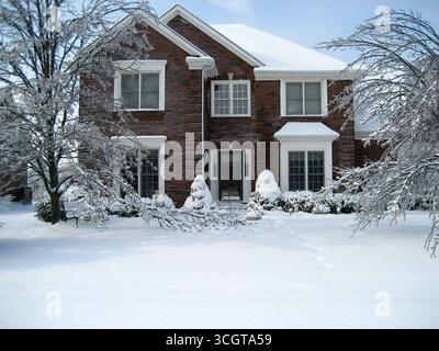 Zweistöckiges Backsteinwohnhaus im Winter mit Schnee auf dem Dach, Bäumen und Boden Stockfoto