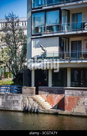Gent, Belgien, 31.03.2025, Ein modernes Apartment am Fluss in Gent, Belgien, mit Glasbalkonen und einer markanten Tauchstatue, die über eine Treppe führt Stockfoto