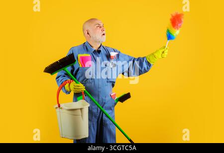Große Reinigung. Ernster Mann in Uniform mit Besen, Staubbürste und Eimer. Professionelle Reinigung. Reiniger in Gummihandschuhen mit Reinigungsmittel. Stecker mit Stockfoto