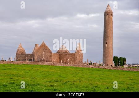 Ein hoher Turm steht vor einer Kirche. Der Turm besteht aus Stein und hat eine spitze Spitze. Die Kirche ist von einem grasbewachsenen Feld umgeben. Der Himmel ist Clo Stockfoto