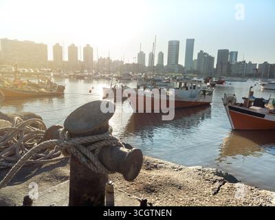 Fischerboote, die bei Sonnenuntergang in einem Hafen in montevideo, uruguay, mit einem Seil, das an einem Schiffspoller im Vordergrund befestigt ist Stockfoto