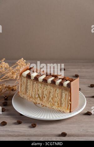 Ein wunderschön präsentiertes Stück Schokolade-Creme-Kuchen auf einem weißen Teller, gestylt mit Kaffeebohnen und getrockneten Blumen vor einem neutralen Hintergrund Stockfoto