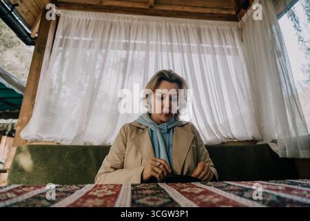 Eine Frau in einem beigen Mantel schaut sich ein kleines schwarzes Objekt an Stockfoto