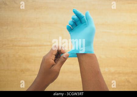 Person, die blaue medizinische Handschuhe in einer sauberen Umgebung anzieht Stockfoto