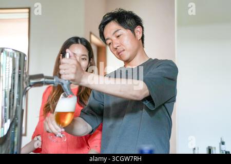 Ein Mann gießt Bier in ein Glas, während eine Frau zusieht. Die Szene ist lässig und entspannt, Mann und Frau genießen die Gesellschaft des anderen Stockfoto