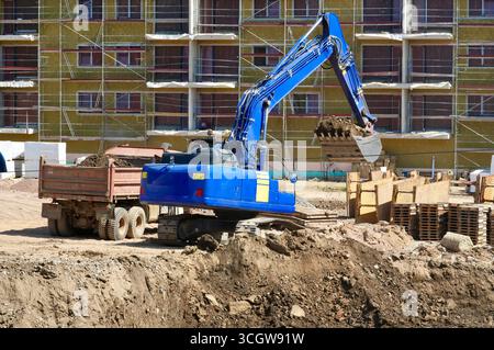 Bagger auf einer Baustelle vor dem Hintergrund von mehrstöckigen Gebäuden Stockfoto