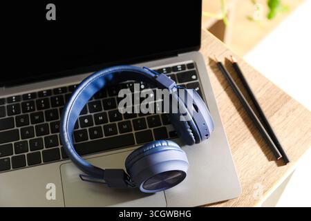 Laptop, kabellose Kopfhörer und Bleistifte auf Holztisch drinnen, Nahaufnahme Stockfoto