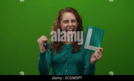 Frau, die mit Freude und Aufregung Autoschlüssel und Lernzeichen vor isoliertem grünem Hintergrund hält. Stockfoto