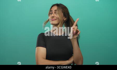 Junge blonde Frau zeigt den Finger in einem grünen Fotostudio nach oben; Selbstvertrauen Verspieltheit Motivation Stärkung. Stockfoto