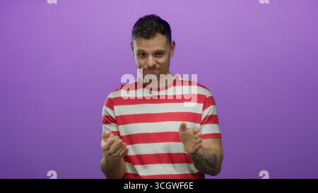 Junger hispanischer Mann in einem rot gestreiften Hemd steht vor einem isolierten lila Hintergrund mit einem durchdachten Ausdruck und ausdrucksstarken Handgesten. Stockfoto